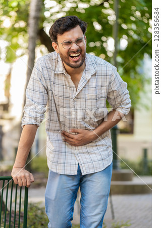 Indian young man traveler feeling sudden strong abdominal stomach ache, gastritis problem on street Indian young man traveler feeling sudden strong abdominal stomach ache, gastritis problem on street 128356684
