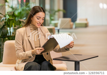 Caucasian young female entrepreneur in formal analyzing graph documents reports in office lobby 128356711