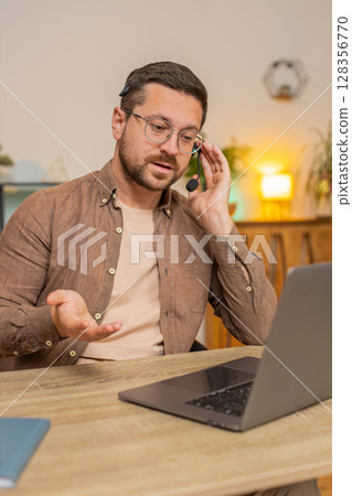Young male customer service representative with headset using laptop computer at home office desk 128356770