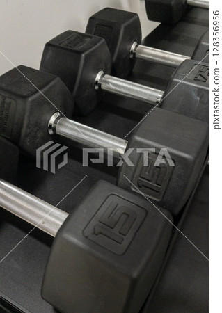 Set of black rubber dumbbells arranged neatly on a gym rack for fitness and strength training 128356956