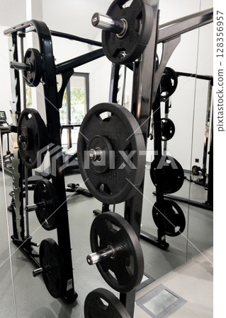 Weightlifting equipment with black plates arranged on a rack in a modern gym environment Weightlifting equipment with black plates arranged on a rack in a modern gym environment 128356957
