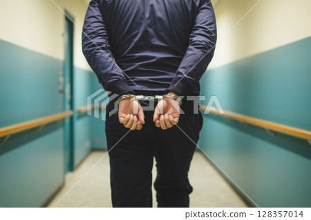 Individual in handcuffs walking down a corridor with teal walls and subdued lighting atmosphere Individual in handcuffs walking down a corridor with teal walls and subdued lighting atmosphere 128357014