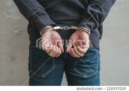 Individual in handcuffs with hands behind back, symbolizing arrest and legal consequences 128357020