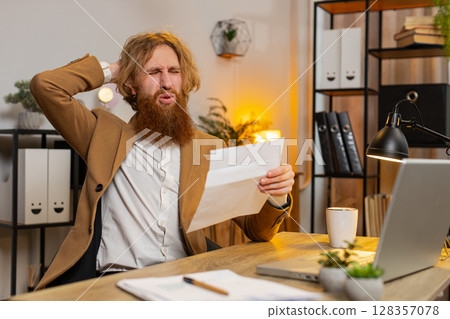 Businessman opening envelope reading bad news in letter feels upset bank debt sitting at office 128357078