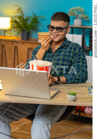 Business man taking break from work wearing 3D glasses eating popcorn and watching movie at office 128357081
