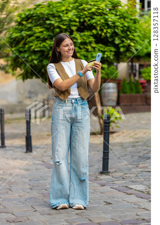 Happy Caucasian woman using credit card smartphone while purchases online shopping on city street 128357118