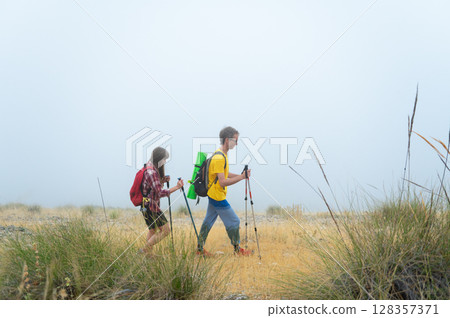 Two Adventurers Exploring Mountain Trails on a Foggy Morning Two Adventurers Exploring Mountain Trails on a Foggy Morning 128357371