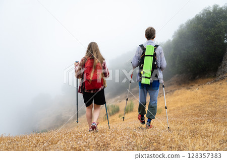 Two Hikers Navigating Through a Foggy Landscape in the Early Morning Two Hikers Navigating Through a Foggy Landscape in the Early Morning 128357383