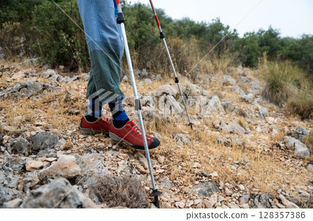 Exploration in Rocky Terrain: Hiker Trekking with Poles and Durable Shoes 128357386