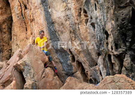 Man Climbing a Rocky Cliff Face in Bright Natural Setting Man Climbing a Rocky Cliff Face in Bright Natural Setting 128357389