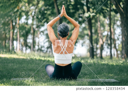 Woman Practicing Seated Raised Hands Pose (Urdhva Hastasana) in a Peaceful Forest Park 128358434