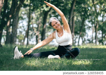 Smiling Woman in Parighasana Side Stretch Yoga Pose Outdoors in a Peaceful Forest Setting 128358435