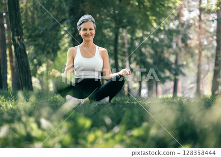 Happy Mature Woman Meditating Outdoors in Sukhasana Pose, Embracing Wellness and Serenity 128358444