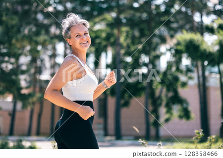 Happy Fit Senior Woman Jogging Outdoors in Sportswear, Smiling and Embracing Active Life 128358466