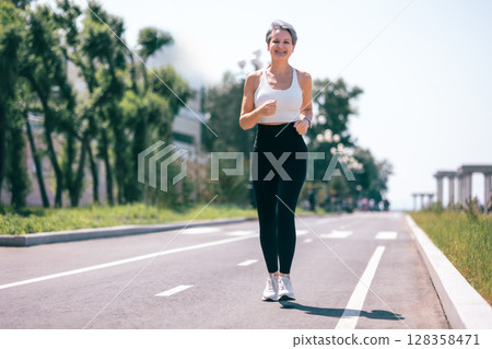 Happy Mature Woman Jogging Outdoors in Activewear on Sunny Day in Urban Park Environment 128358471