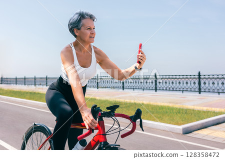 Senior Woman on Bicycle Taking Selfie with Smartphone While Riding Along Seafront Senior Woman on Bicycle Taking Selfie with Smartphone While Riding Along Seafront 128358472