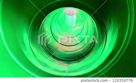 Experience the rush of a green water slide twisting through a glowing tube, as a daring individual slides down illuminated by vibrant lights 128358776