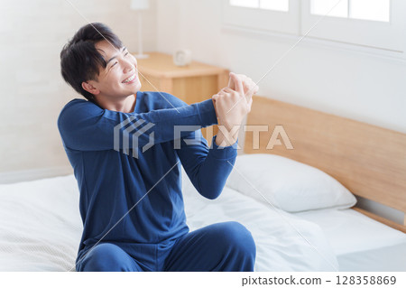 A man gets up from bed in the morning and stretches 128358869