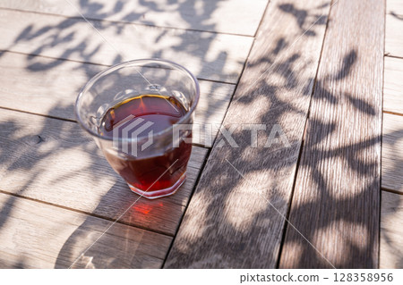 [日本] 陽光透過樹梢，在露台的木桌上，用玻璃杯喝著黑咖啡 128358956