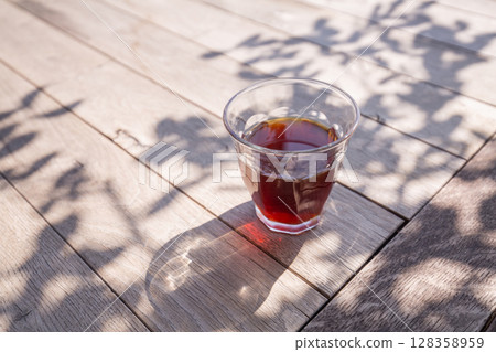 [日本] 陽光透過樹梢，在露台的木桌上，用玻璃杯喝著黑咖啡 128358959