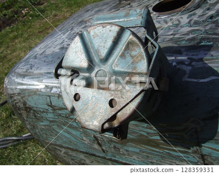 A close-up view of a worn machinery component revealing rust and corrosion. The part is situated on a metallic surface in a grassy outdoor area, reflecting age and usage. 128359331