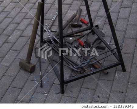 A collection of metal tools and hardware is displayed on a black iron stand in a workshop space. The tools show signs of use, reflecting a working environment. 128359342