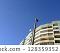 A residential building stands under a bright blue sky, with a streetlight and satellite dish visible. This captures vibrant urban life in a daylight setting, highlighting city design. 128359352