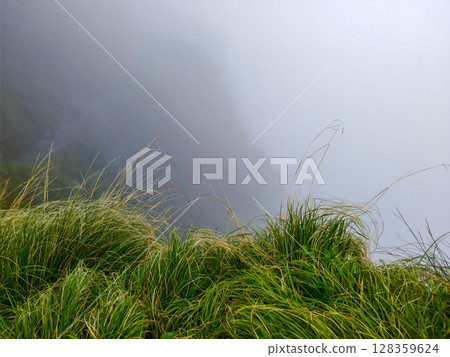 Misty Cliffside Grassland with Ethereal Fog and Rugged Terrain 128359624