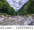 Rocky Riverbed in Forest Valley Under Cloudy Sky 128359651