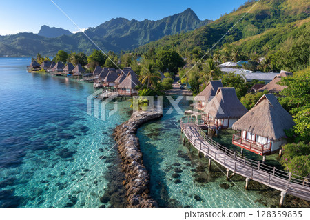 Aerial View of Vibrant Turquoise Lagoon with Lining Bungalows Surrounded by Lush Mountains 128359835