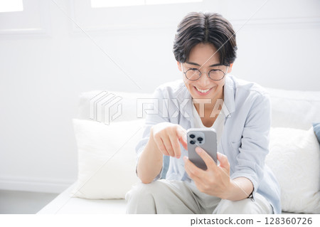 特寫:一位戴著眼鏡的英俊男子在一間漂亮的房間裡看著、拿著並敲擊著智慧型手機 特寫:一位戴著眼鏡的英俊男子在一間漂亮的房間裡看著、拿著並敲擊著智慧型手機 128360726