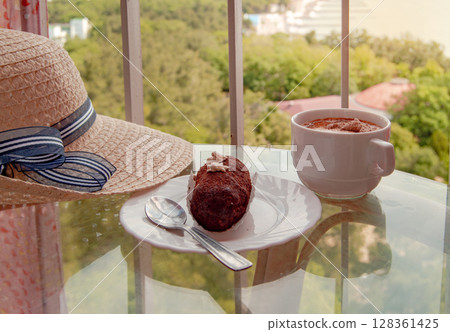Vintage still life with a woman's hat, a cup of coffee and a brownie on a glass table Vintage still life with a woman's hat, a cup of coffee and a brownie on a glass table 128361425