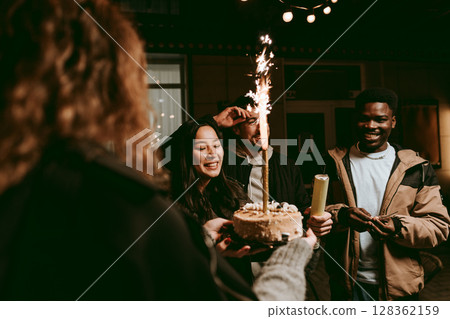 Friends celebrating a birthday with a cake and sparklers in a cozy outdoor setting at night Friends celebrating a birthday with a cake and sparklers in a cozy outdoor setting at night 128362159