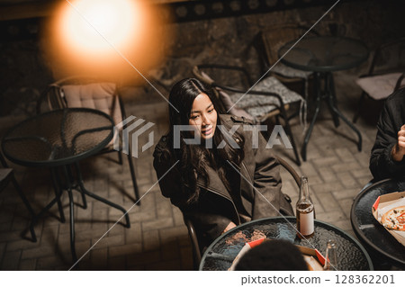 Group enjoys evening gathering at outdoor cafe with drinks and pizza on cozy night in urban setting Group enjoys evening gathering at outdoor cafe with drinks and pizza on cozy night in urban setting 128362201
