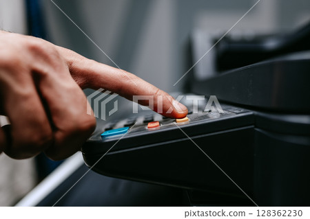 Person pressing buttons on office equipment in a busy workspace during the day Person pressing buttons on office equipment in a busy workspace during the day 128362230
