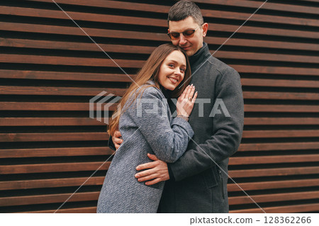 Couple embraces affectionately while posing against a wooden wall in a cozy urban setting during autumn Couple embraces affectionately while posing against a wooden wall in a cozy urban setting during autumn 128362266