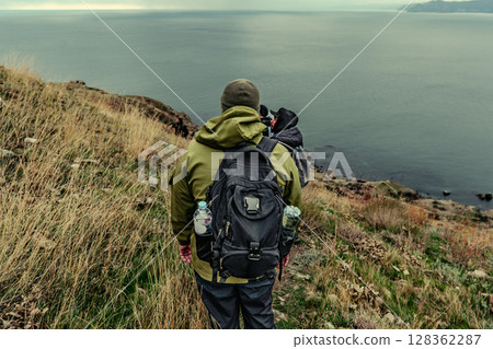 Hiker overlooking the calm waters of a distant coastline during a cloudy afternoon 128362287