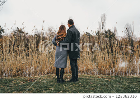 Couple enjoying a quiet moment by the water surrounded by tall grass on a cloudy day 128362310