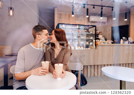 Couple enjoys drinks in cozy cafe during afternoon, engaging in sweet conversation and affectionate moments 128362320