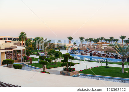 Scenic beachfront resort with palm trees and landscaped gardens at sunset overlooking the ocean 128362322