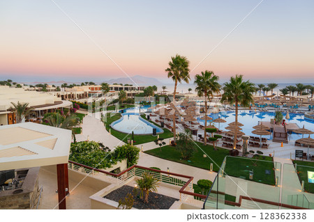Expansive view of a resort with swimming pools and palm trees during sunset Expansive view of a resort with swimming pools and palm trees during sunset 128362338