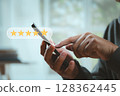Close-up of hands giving a five-star rating on smartphone screen. Concept of online review, user experience, digital reputation, and customer satisfaction. 128362445