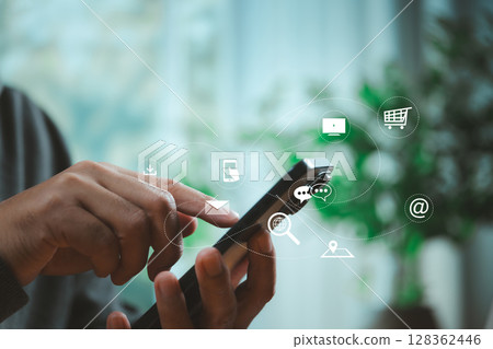 Person using smartphone with floating digital app icons representing cloud services, messaging, shopping, and online business technology in modern lifestyle. Person using smartphone with floating digital app icons representing cloud services, messaging, shopping, and online business technology in modern lifestyle. 128362446