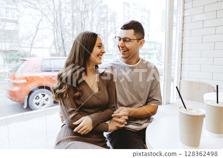Couple sharing a joyful moment at a cafe on a sunny day in the city while enjoying drinks together 128362498