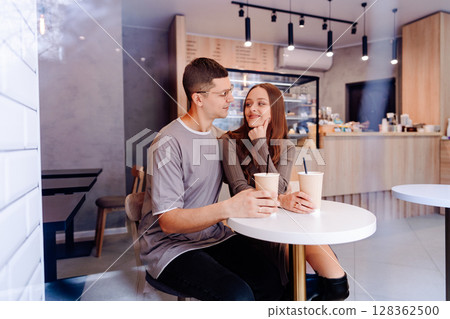 Couple enjoys beverages at a modern cafe in the afternoon while sharing smiles and conversation together 128362500