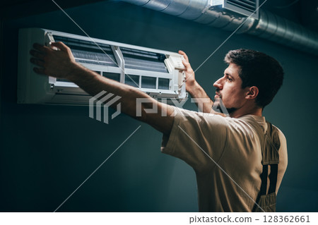 Technician installs air conditioning unit in residential space during daylight hours Technician installs air conditioning unit in residential space during daylight hours 128362661