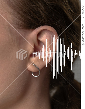 Captivating close-up of an ear adorned with a fashionable earring while sound waves visually illustrate the beauty of hearing 128362729