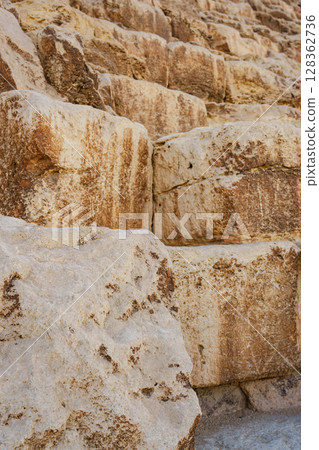 Large ancient limestone blocks form the base of a historical structure in the desert, showcasing impressive quarrying techniques used in construction Large ancient limestone blocks form the base of a historical structure in the desert, showcasing impressive quarrying techniques used in construction 128362736