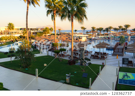 Luxurious resort pool area with palm trees and sun loungers near the ocean at sunset in a tropical location 128362737