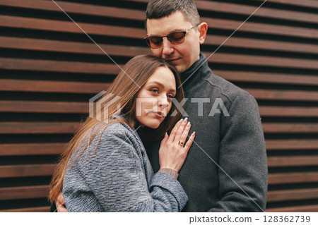 Couple sharing a warm embrace against a wooden backdrop on a cool day in a city setting 128362739